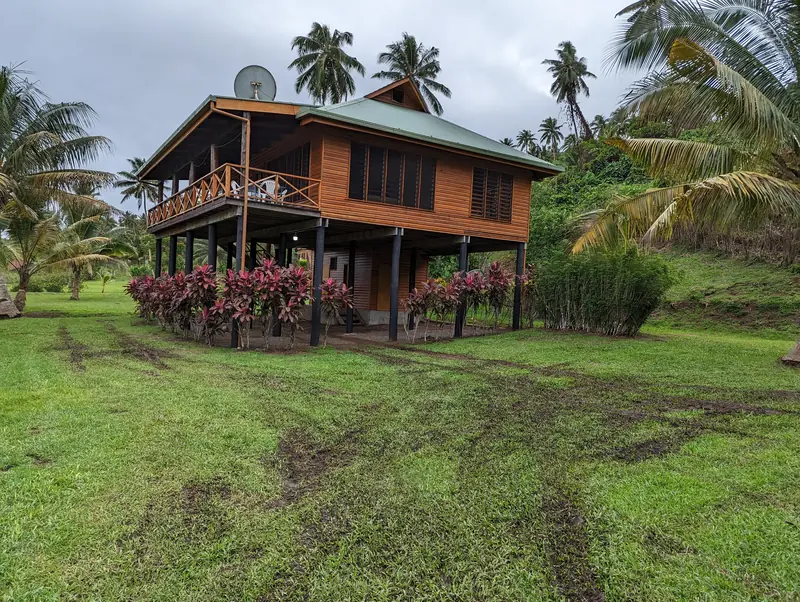 The two-storey timber house in its garden with palms